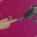 two hands touching each other in front of a pink background